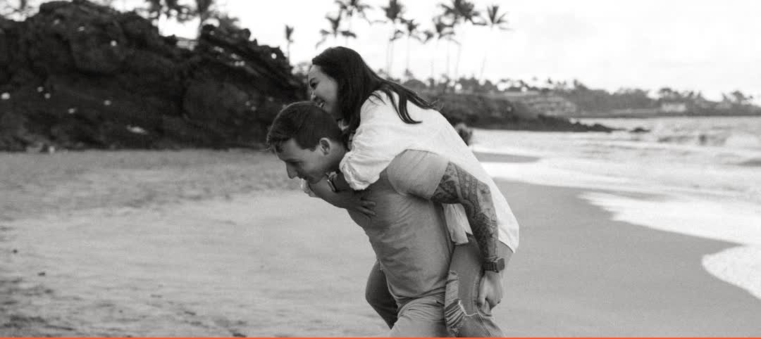 Tanner carrying his wife on his back on a Maui beach, black and white photo